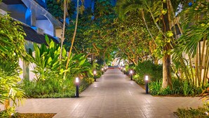 A pathway lined with trees and illuminated by ground lights, leading to a building with a modern design. - Pooh Beach Resort & Spa (Pattaya)