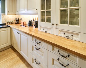 A kitchen with white cabinets, a wooden countertop, and a coffee maker. - Chapel Cottage (Barnard Castle)