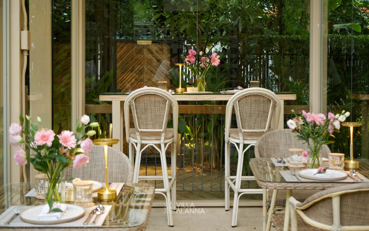 A dining area with wicker chairs, a glass table, and floral centerpieces.