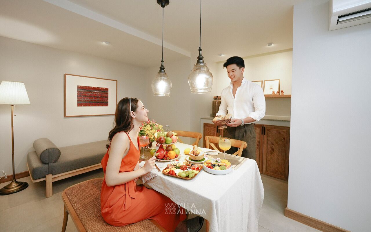 A dining area with a table set for two, a sofa, and a lamp.