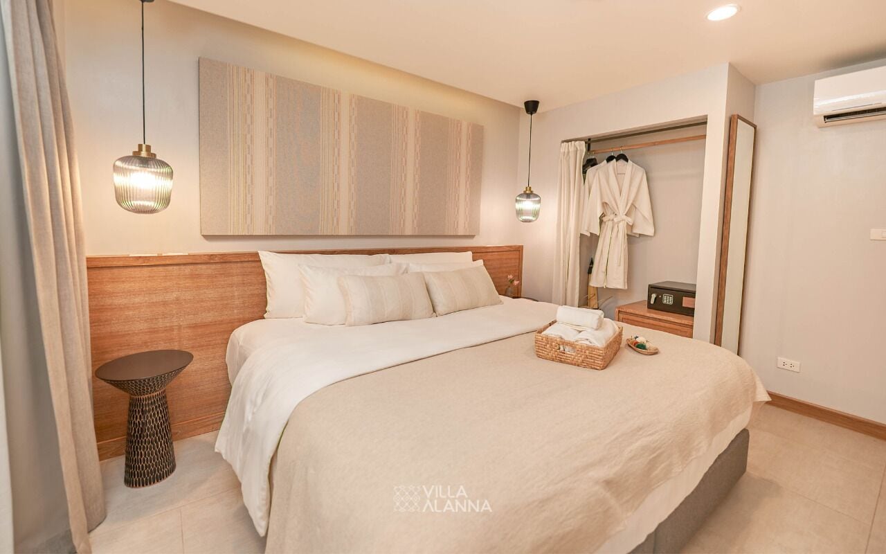 Quarto de hotel moderno com uma cama grande, uma mesinha de cabeceira, uma obra de arte na parede, um roupão pendurado em um suporte e um aparelho de ar condicionado.
