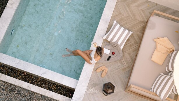 A woman relaxing by a poolside with a drink, surrounded by a lounge area with striped cushions and a wooden floor. - Villa ALANNA (Chiang Mai)