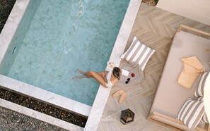 A woman relaxing by a poolside with a drink, surrounded by a lounge area with striped cushions and a wooden floor. - Villa ALANNA (Chiang Mai)