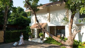 A white villa with a tiled roof, a large tree in front, and a paved driveway. - Villa ALANNA (Chiang Mai)