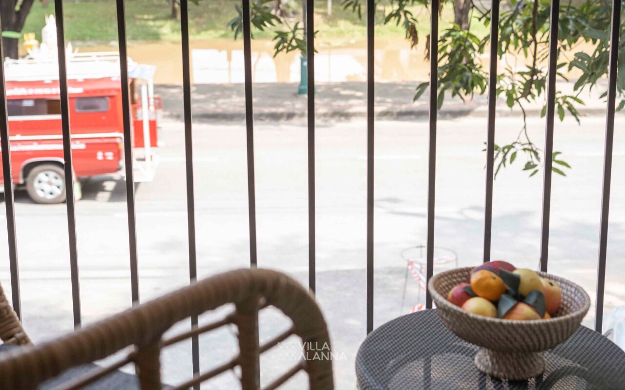 A view through a metal gate with a wicker chair and a table with a fruit bowl.
