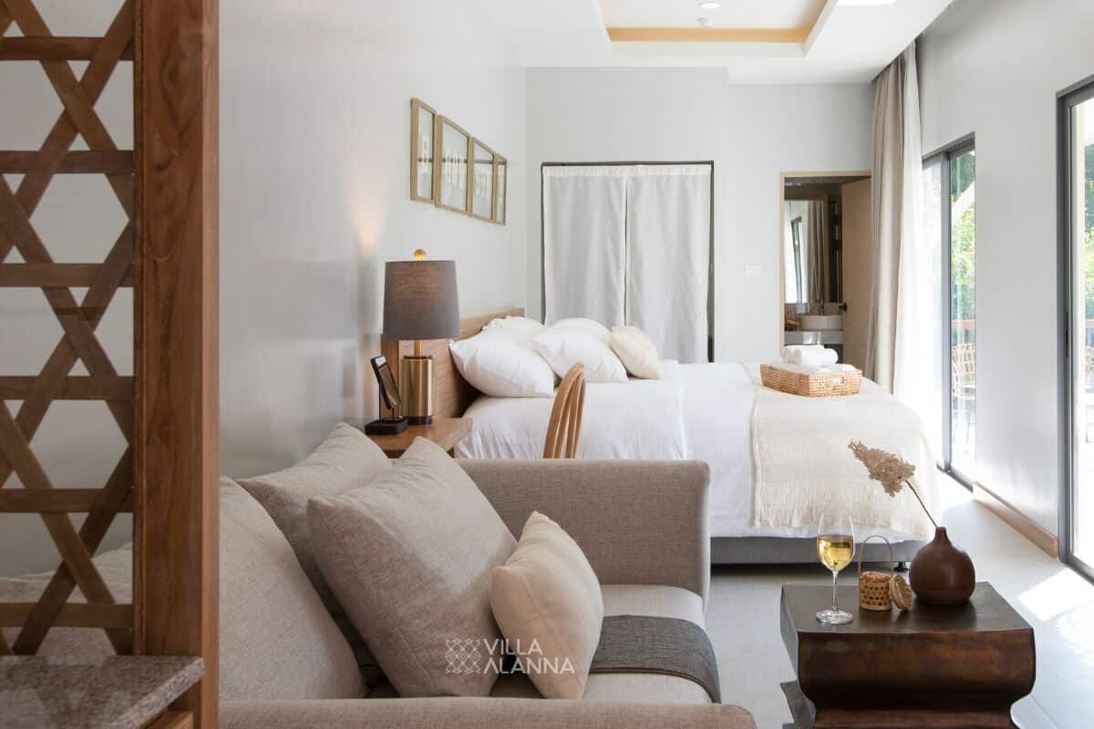 Una habitación de hotel moderna con una cama, un sofá, una mesita de noche y un ventanal grande.