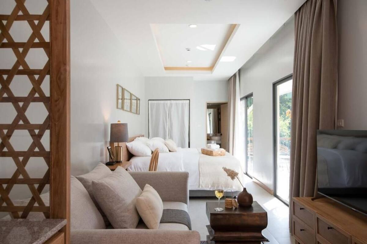 Una habitación de hotel moderna con cama, sofá, televisión y ventanas amplias.