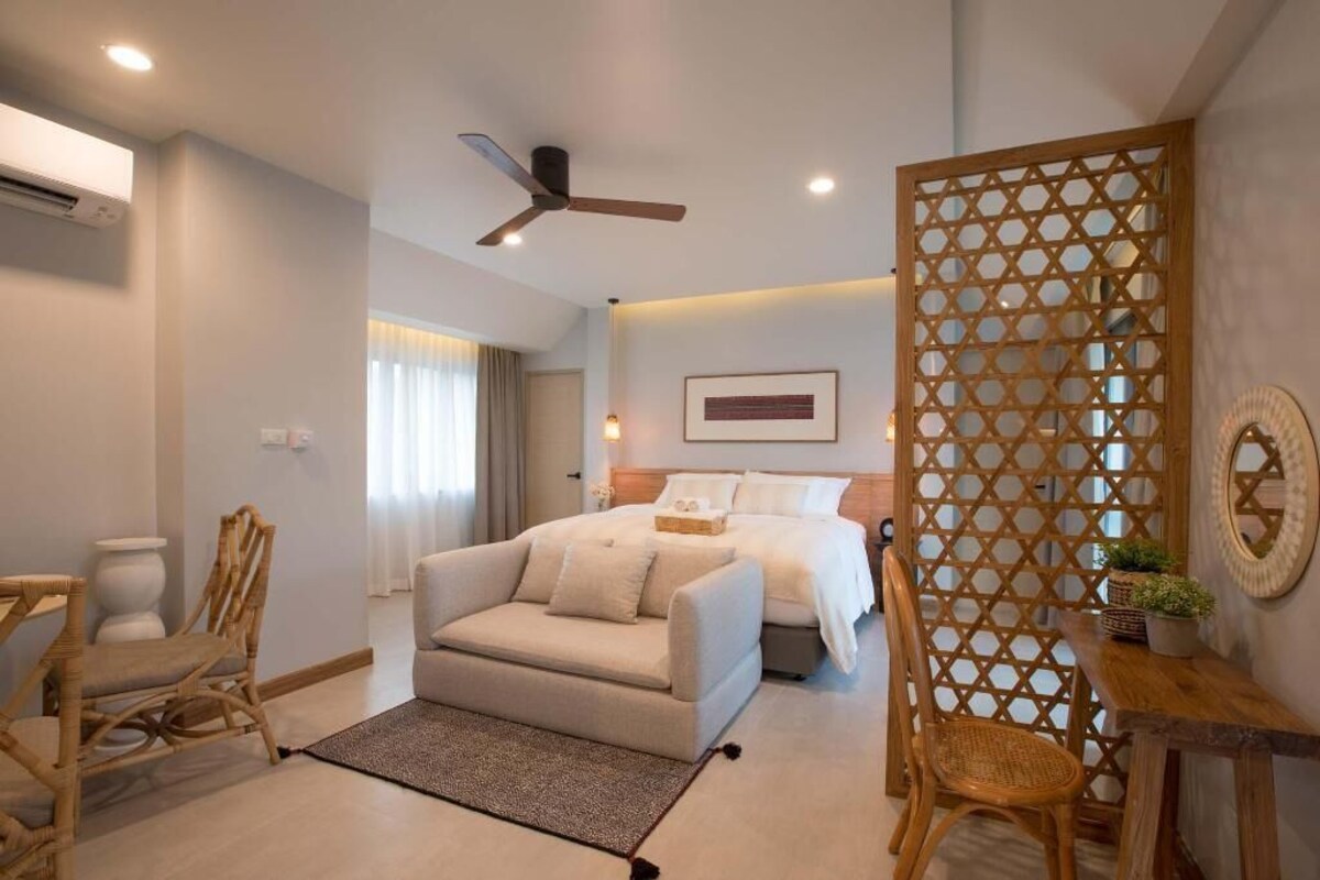 A bedroom with a bed, a desk, a chair, a ceiling fan, and a decorative wooden partition.