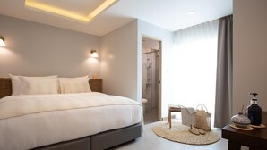 A modern bedroom with a large bed, bedside lamps, a small table with a bottle, and a chair. - Villa ALANNA (Chiang Mai)