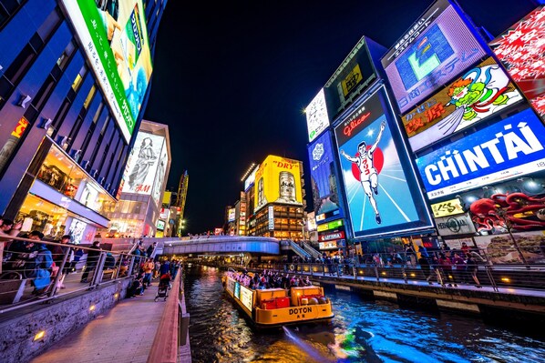 Uma área urbana bem iluminada, com um rio, um barco e diversos outdoors iluminados.