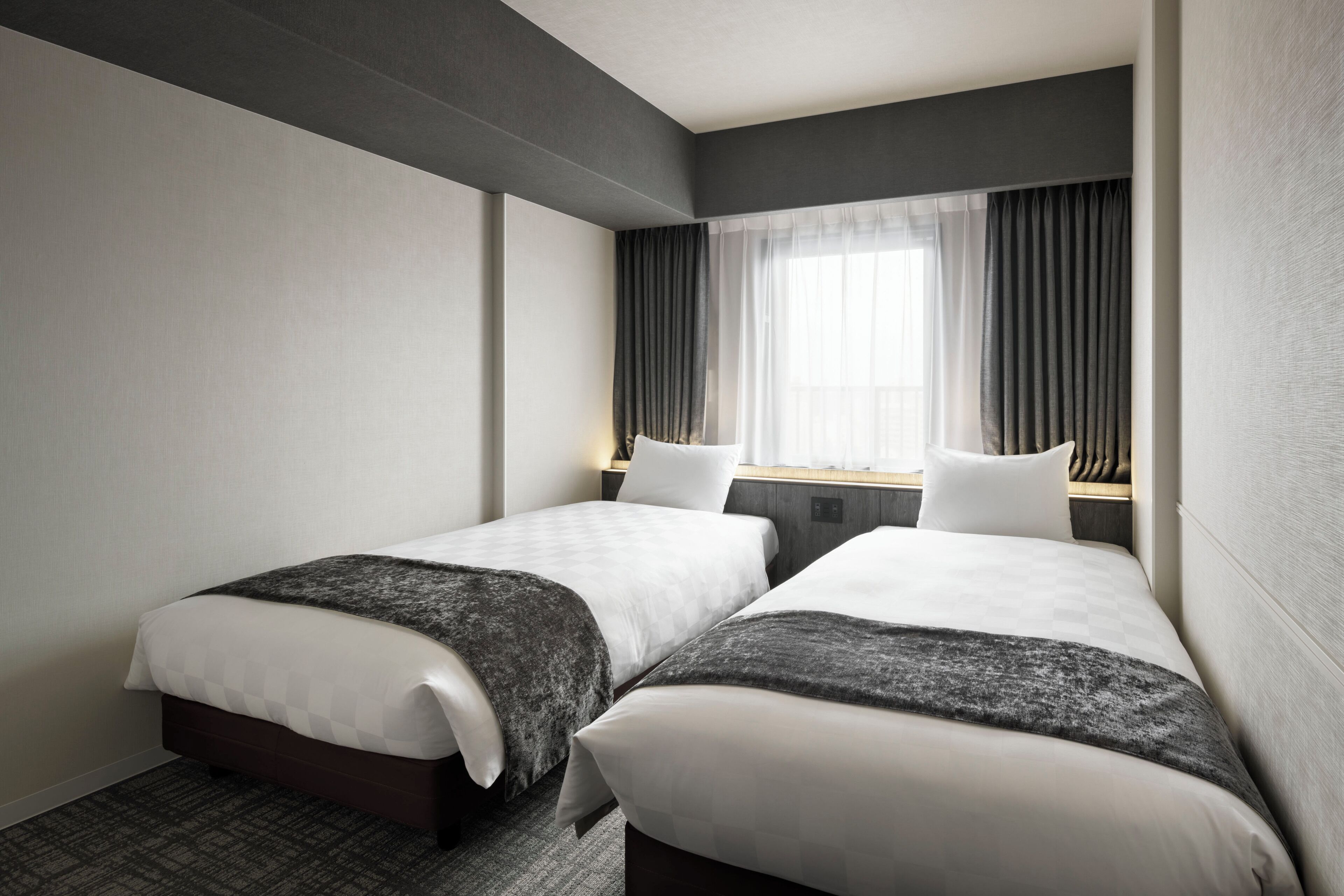Habitación de hotel con dos camas, un ventanal con cortinas y una alfombra a cuadros.