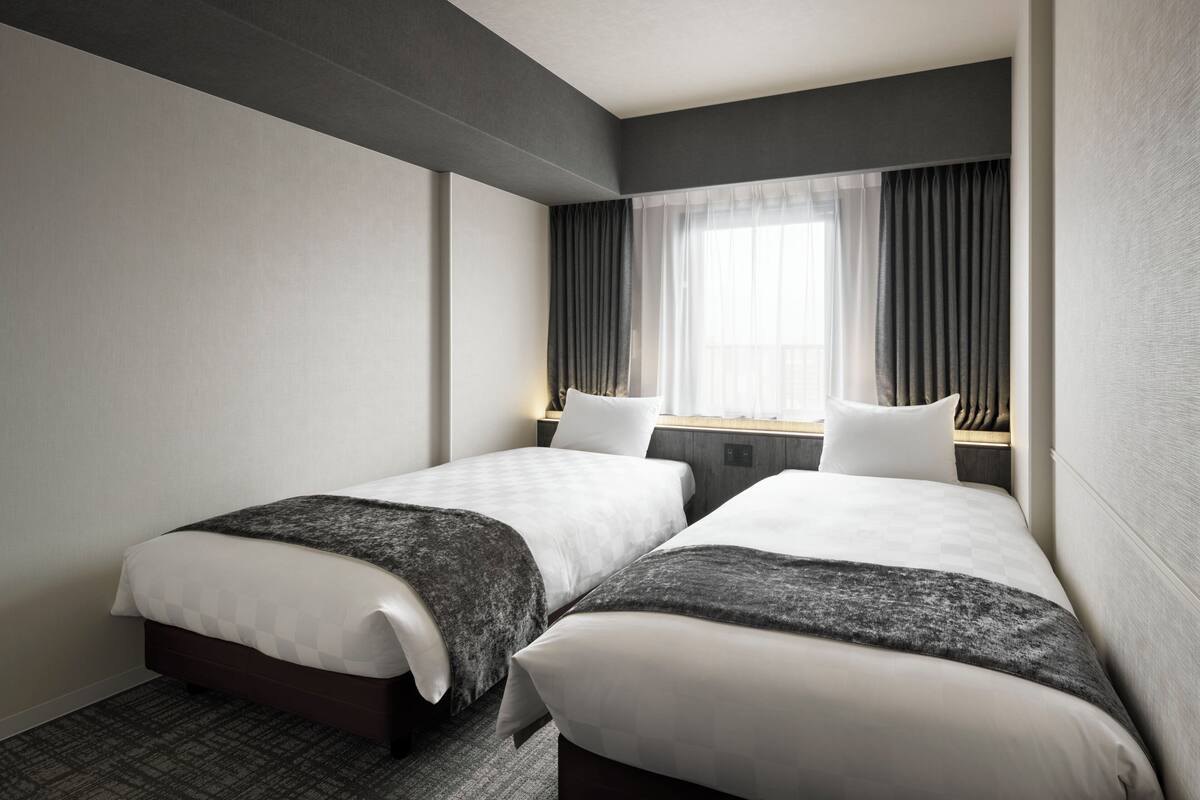 Habitación de hotel con dos camas, un ventanal con cortinas y una alfombra a cuadros.