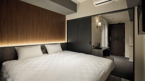A modern hotel room with a large bed, a wooden headboard, a dark wardrobe, a small desk with a lamp, and a mirror. - The Onefive Osaka Shinsekai (Osaka)