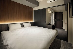 A modern hotel room with a large bed, a wooden headboard, a dark wardrobe, a small desk with a lamp, and a mirror. - the b Osaka-shinsekai (Osaka)