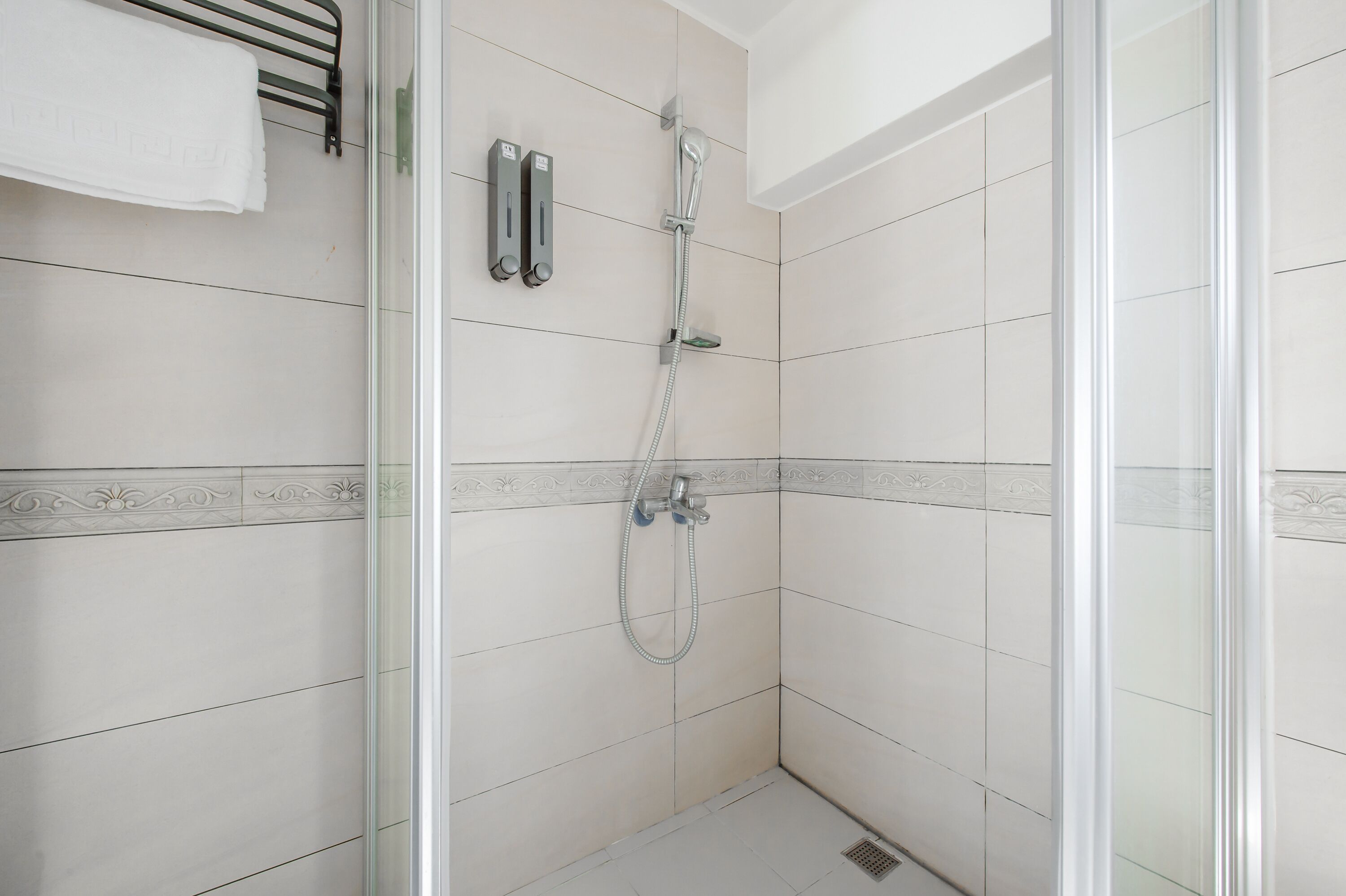 A shower area with a glass door, white tiled walls, and a towel rack.