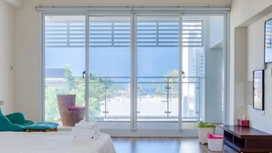 A hotel room with a large sliding glass door leading to a balcony, a bed with white linens, a teal chair, and a small table with a pink object. - White House (Liuqiu)