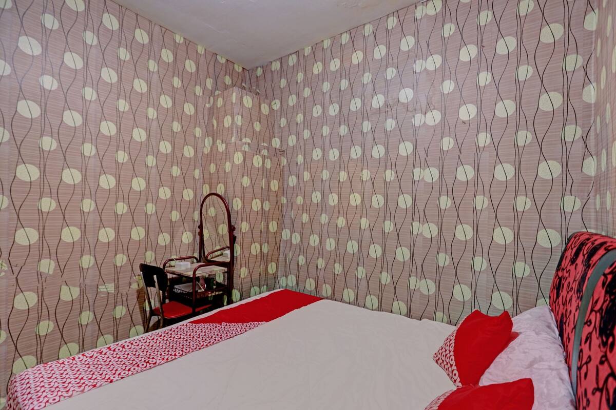 Une chambre à coucher avec un lit, une chaise et une table. Les murs sont décorés d’un motif de feuilles.