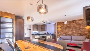 Un espace de vie moderne comprenant un coin repas avec une table en bois et des chaises noires, une cuisine en arrière-plan et un mur d’accent en bois.