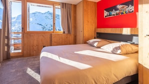 Une chambre avec un grand lit, des murs en bois, un mur d’accent rouge et une fenêtre donnant sur les montagnes.