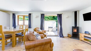 A spacious living room with a fireplace, a dining area with wooden furniture, and large windows allowing natural light. - Chy Pol (Wadebridge)
