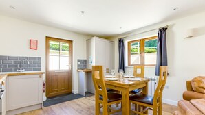 A compact kitchen with a dining table set for four, wooden chairs, a built-in oven, and a window with curtains. - Chy Pol (Wadebridge)