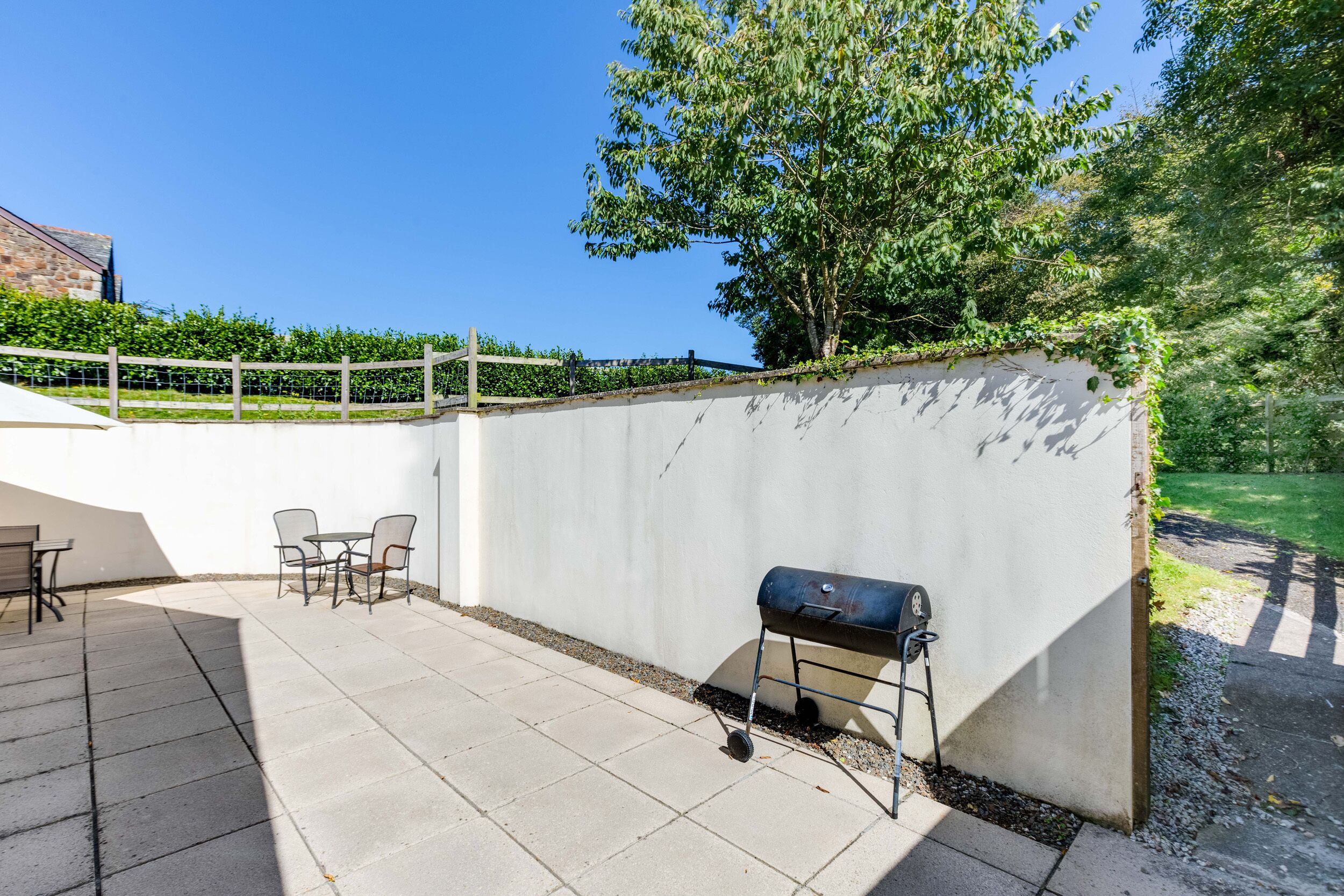 An outdoor patio with a barbecue grill, seating area, and a white wall.