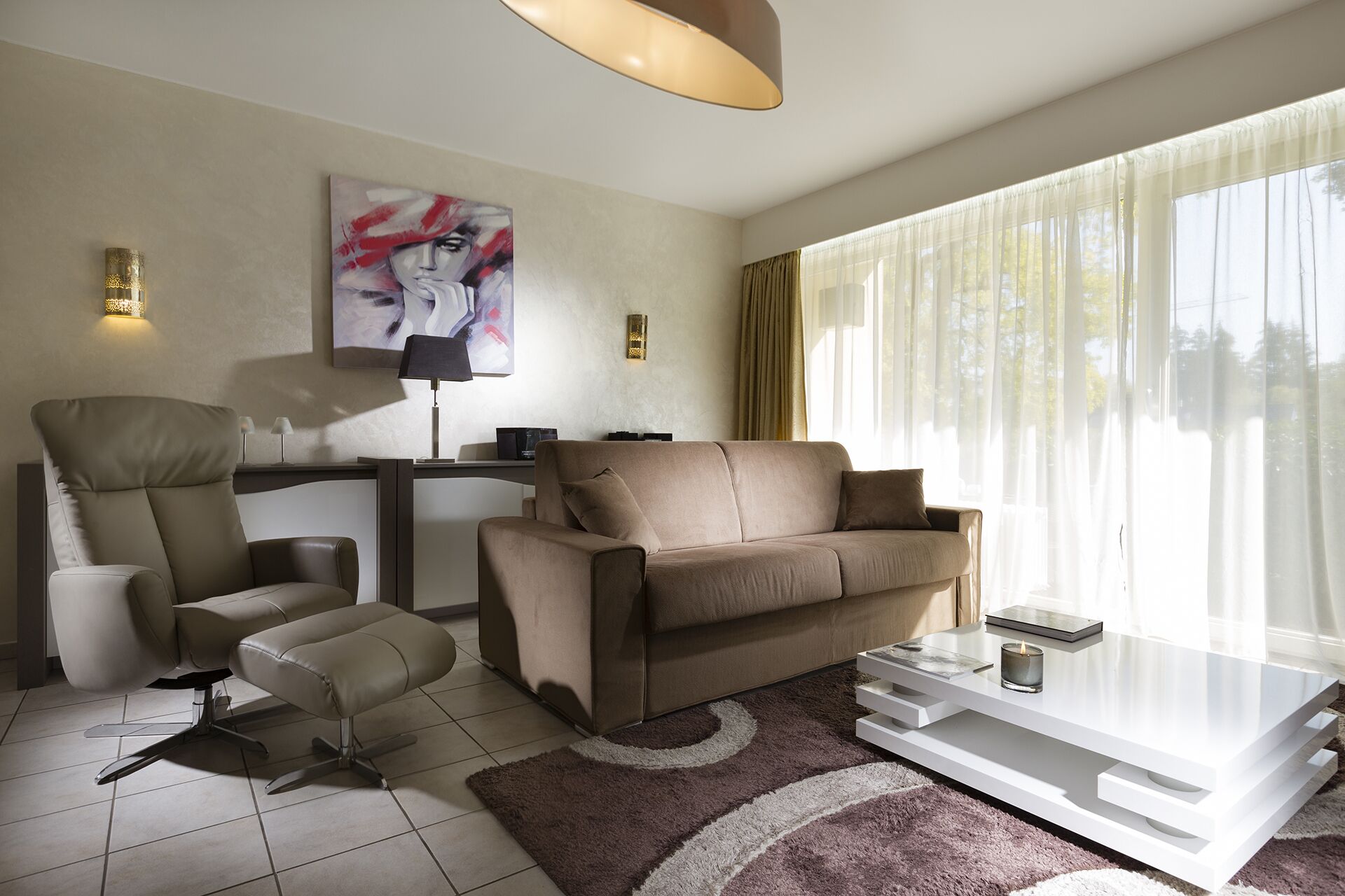 Ein modernes Wohnzimmer mit einer Couch, einem Sessel, einem Hocker, einem Couchtisch und einem Bild an der Wand.