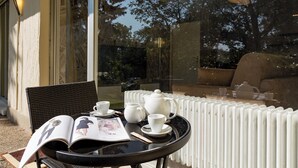 Ein Tisch mit Zeitschrift, Tee-Service und einem Stuhl vor einem Gebäude mit großen Fenstern.