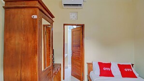 Ein Schlafzimmer mit einem Holzschrank, einem Bett mit roten Kissen und einer weißen Klimaanlage an der Wand.