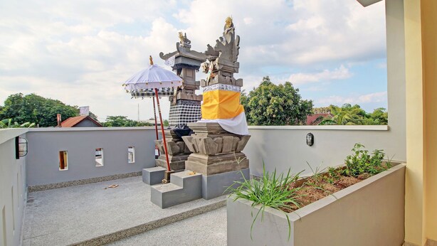 Eine Dachterrasse mit einer Steinstatue, einem kleinen Sonnenschirm und einem Blumentopf mit Grünpflanzen.