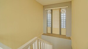 Eine schmale Treppe mit weißer Geländer, beigen Wänden und einem Fenster mit dekorativem Gitter.
