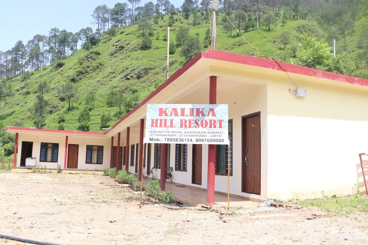 A building labeled "Kalika Hill Resort" with a signboard displaying the name and contact information.