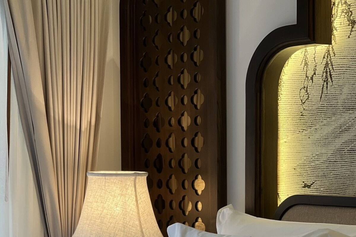 Ein Hotelzimmer mit einem ordentlich bezogenen Bett, einer Lampe und einem dekorativen Kopfteil.
