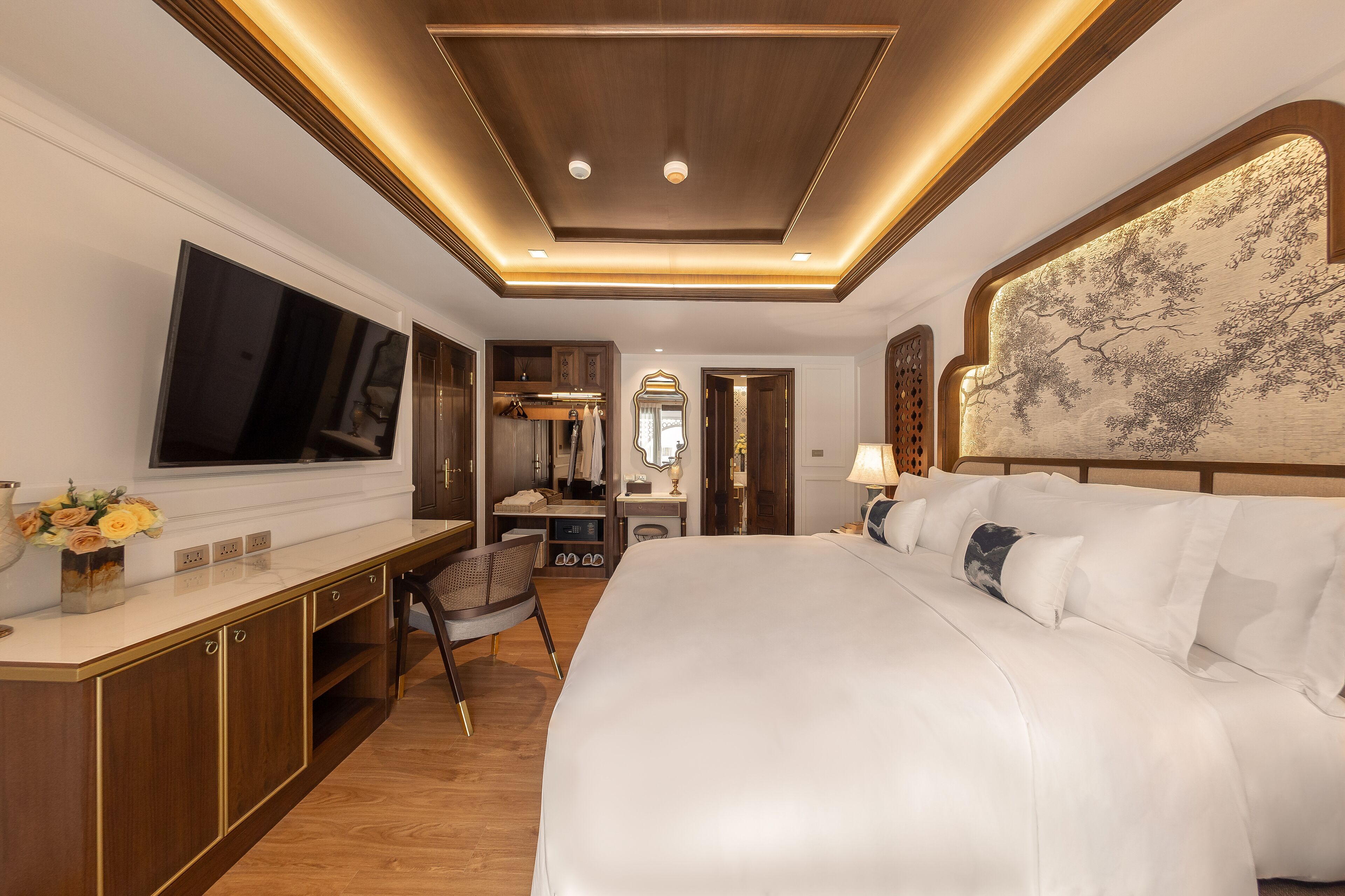 Una camera d'albergo con un letto grande, una scrivania con TV a schermo piatto, una toeletta con specchio e un'opera d'arte appesa al muro.