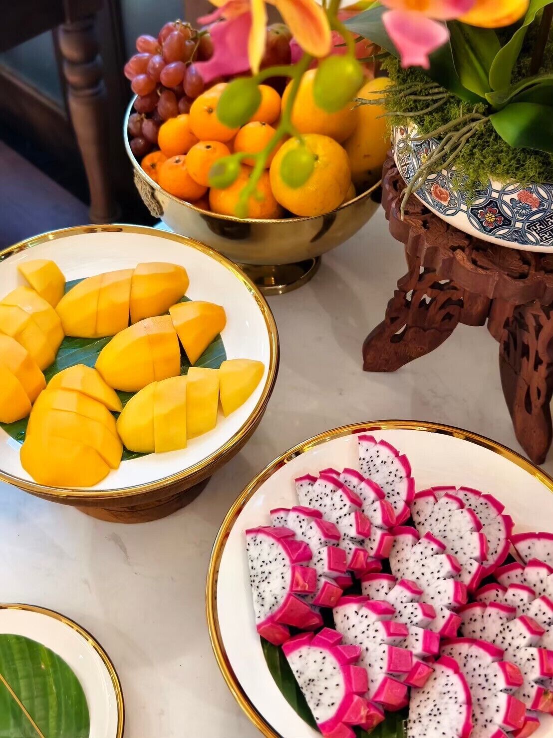 Uma mesa com tigelas de manga fatiada, pitaya e uma tigela de laranjas e uvas.
