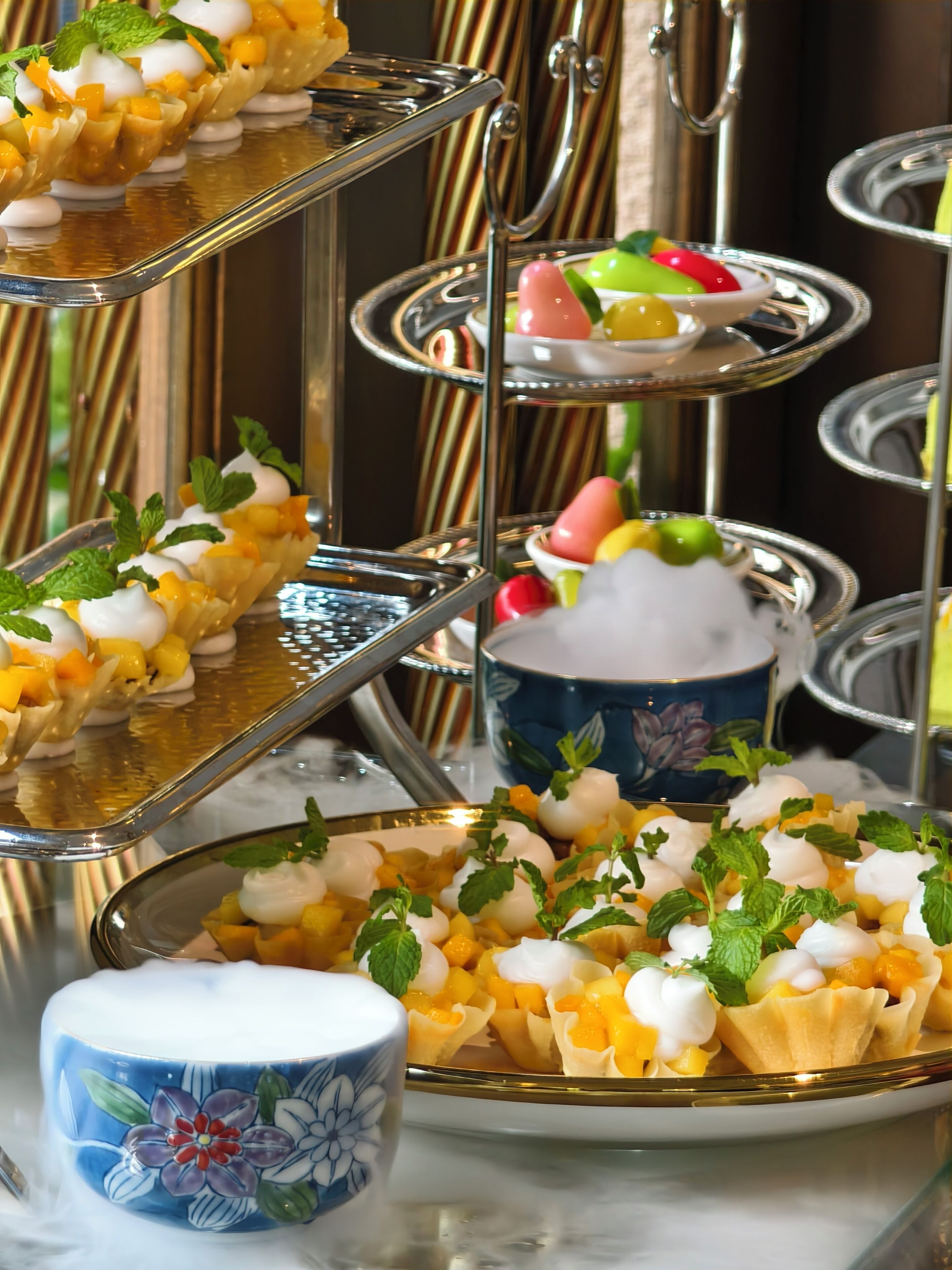 A three-tiered dessert stand with various fruit and cream desserts, a floral-patterned mug, and a decorative background.