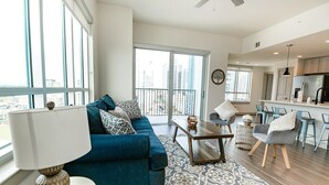 A modern living room with a blue sofa, a coffee table, and a dining area with chairs.