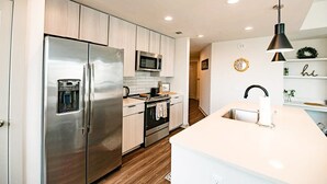 A modern kitchen with stainless steel appliances, wooden cabinets, and a white countertop.