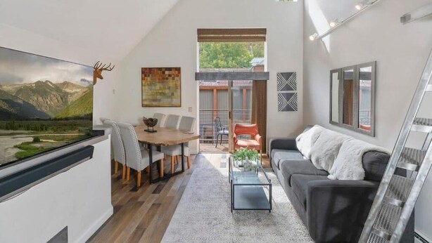 A modern living room with a dining area, a sofa, a coffee table, and a TV mounted on the wall. - Awesome Views; Ski In/Out & lift is 100 steps from the Door (Telluride)