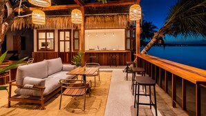 An outdoor seating area with a wooden table, a sofa, and a bar counter. - The Flow Samui Beach Resort (Koh Samui)