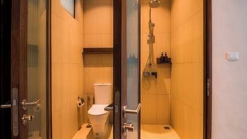 Un baño moderno con ducha de vidrio, inodoro y repisa con artículos de aseo.