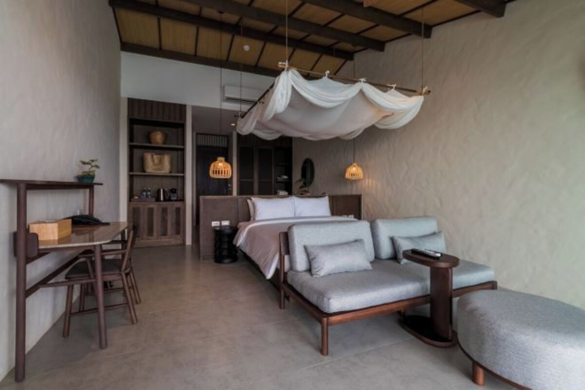 A modern bedroom with a sofa bed, a small table, and a hanging light fixture.