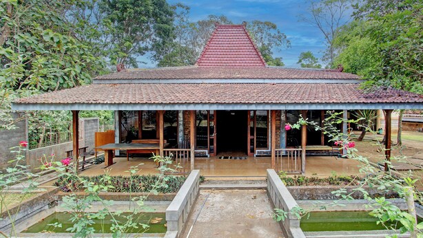 Ein traditionelles Gebäude mit einem Ziegeldach, einer Veranda und einem Garten mit Wasserspielen.