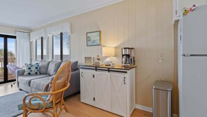 A living room with a sofa, a wicker chair, a cabinet, and a coffee maker. - Ocean Forest Villas Unit E210 - Oceanfront (Myrtle Beach)