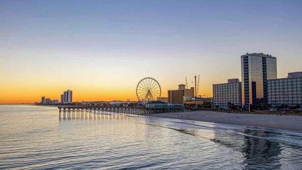 A coastal cityscape with a prominent Ferris wheel, modern high-rise buildings, and a pier extending into the water. - Ocean Forest Villas Unit E210 - Oceanfront (Myrtle Beach)