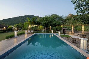 Una piscina rectangular con borde de azulejos, rodeada por una terraza de piedra y faroles decorativos.