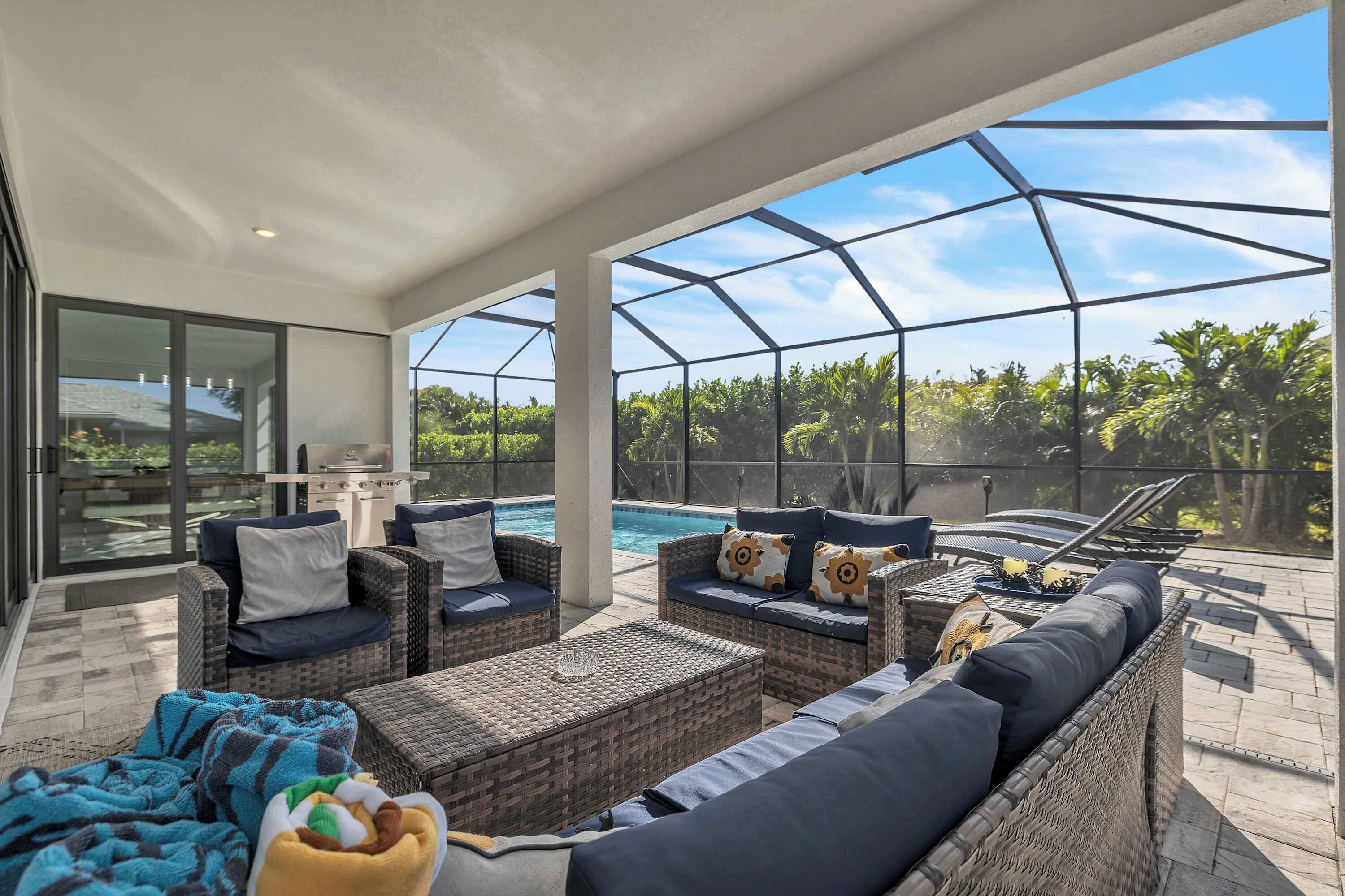 A covered outdoor seating area with wicker furniture, a grill, and a view of a swimming pool.