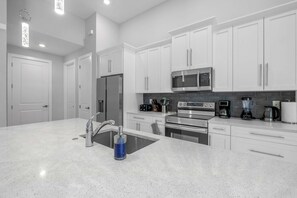 A modern kitchen with white cabinetry, stainless steel appliances, and a granite countertop. - Modern Escape - Pet Friendly,  Salt Pool, 6 Cart ERV (Cape Coral)