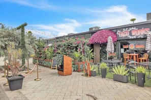 Un restaurant doté d’une terrasse, une enseigne indiquant « Taco Works », ainsi que diverses plantes en pot et de la verdure.
