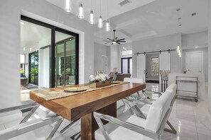 Un espace repas moderne avec une table en bois, des chaises blanches et un ventilateur de plafond.